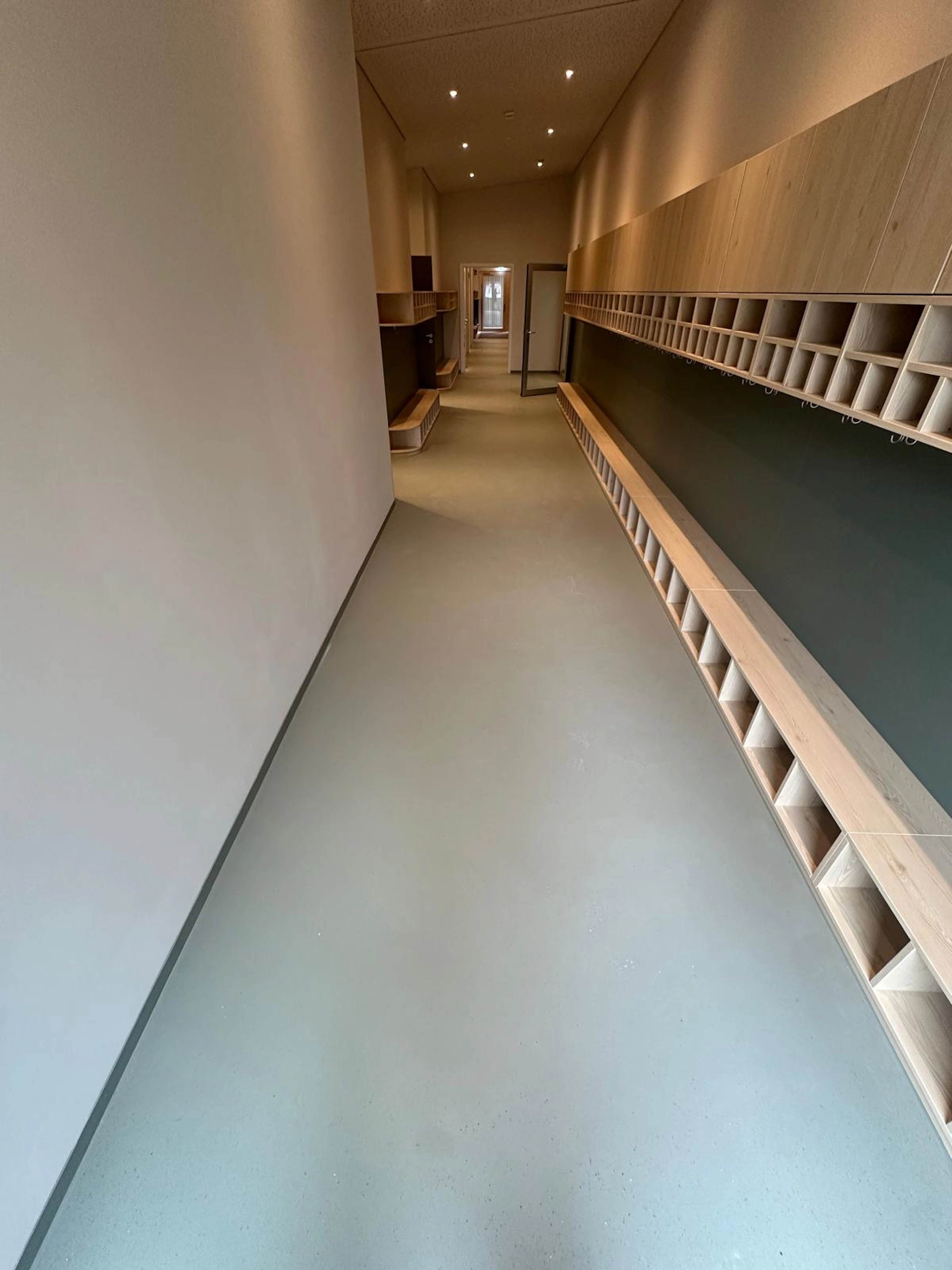 Grauer Bodenbelag in langem Flur mit hellen Holzregalen und Garderoben