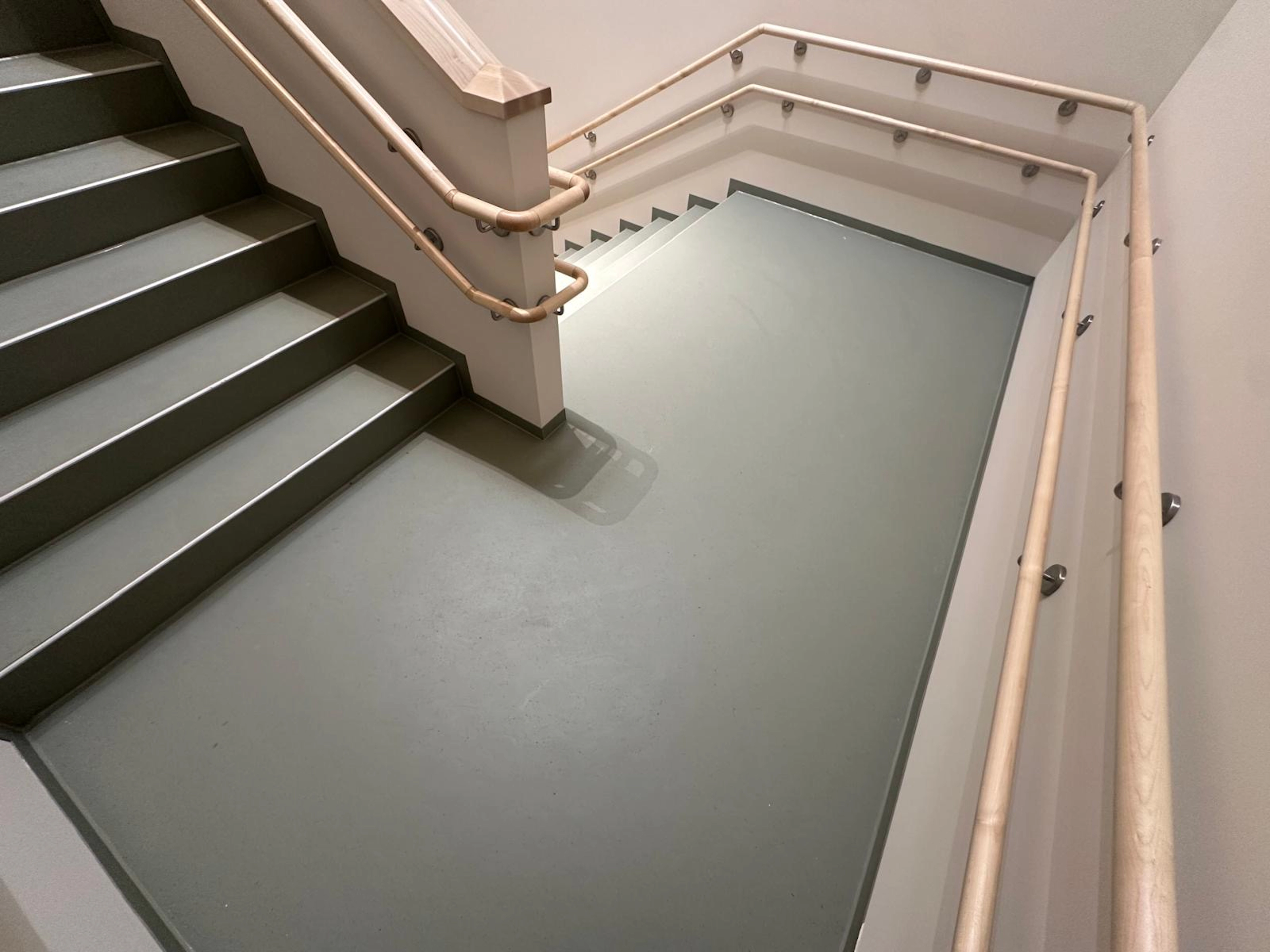 Moderner Treppenaufgang mit grauem Boden und ergonomischen Holzhandläufen