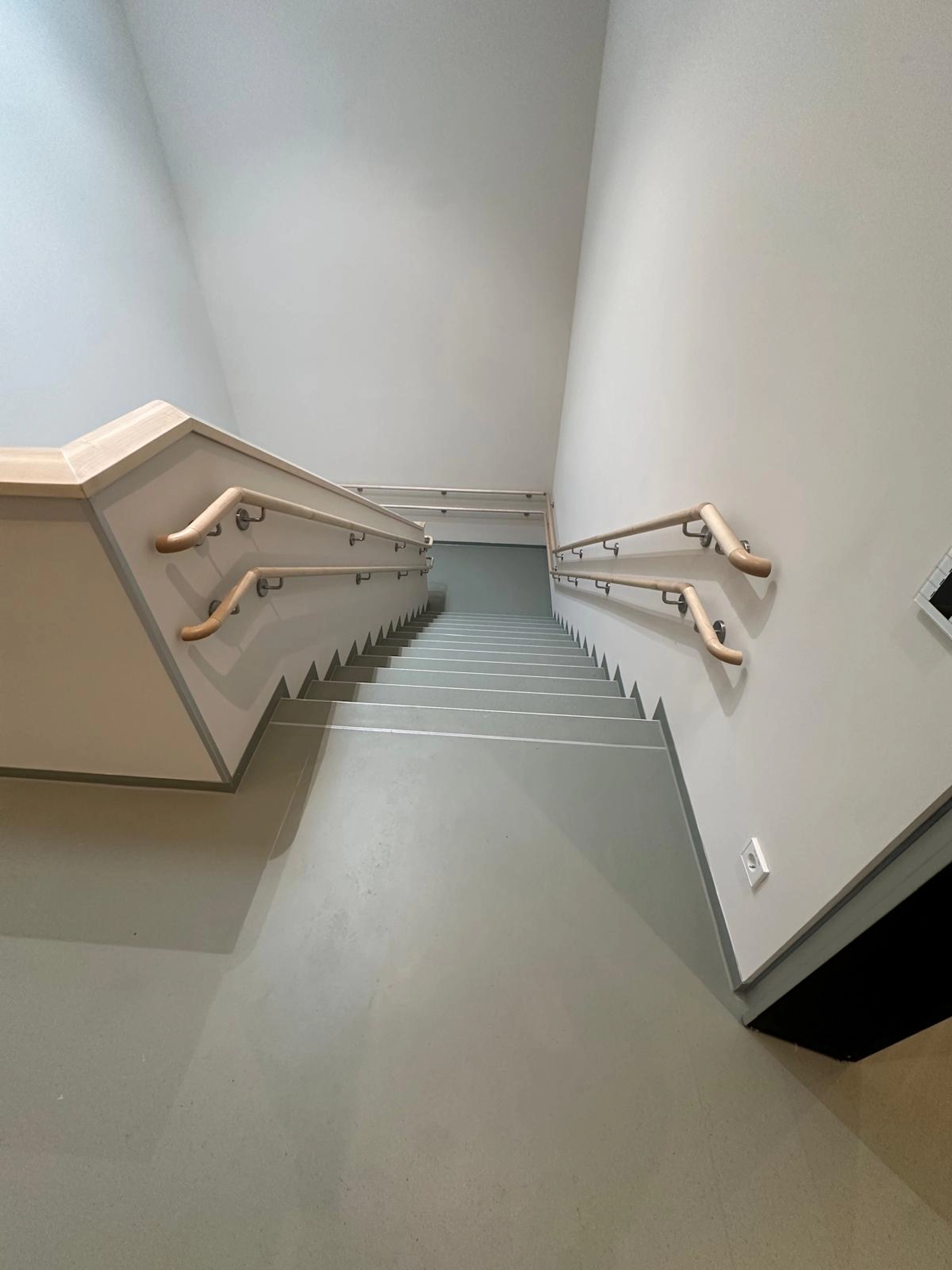 Blickfang Treppe mit grauem Belag und durchgehenden Wandhandläufen aus Holz