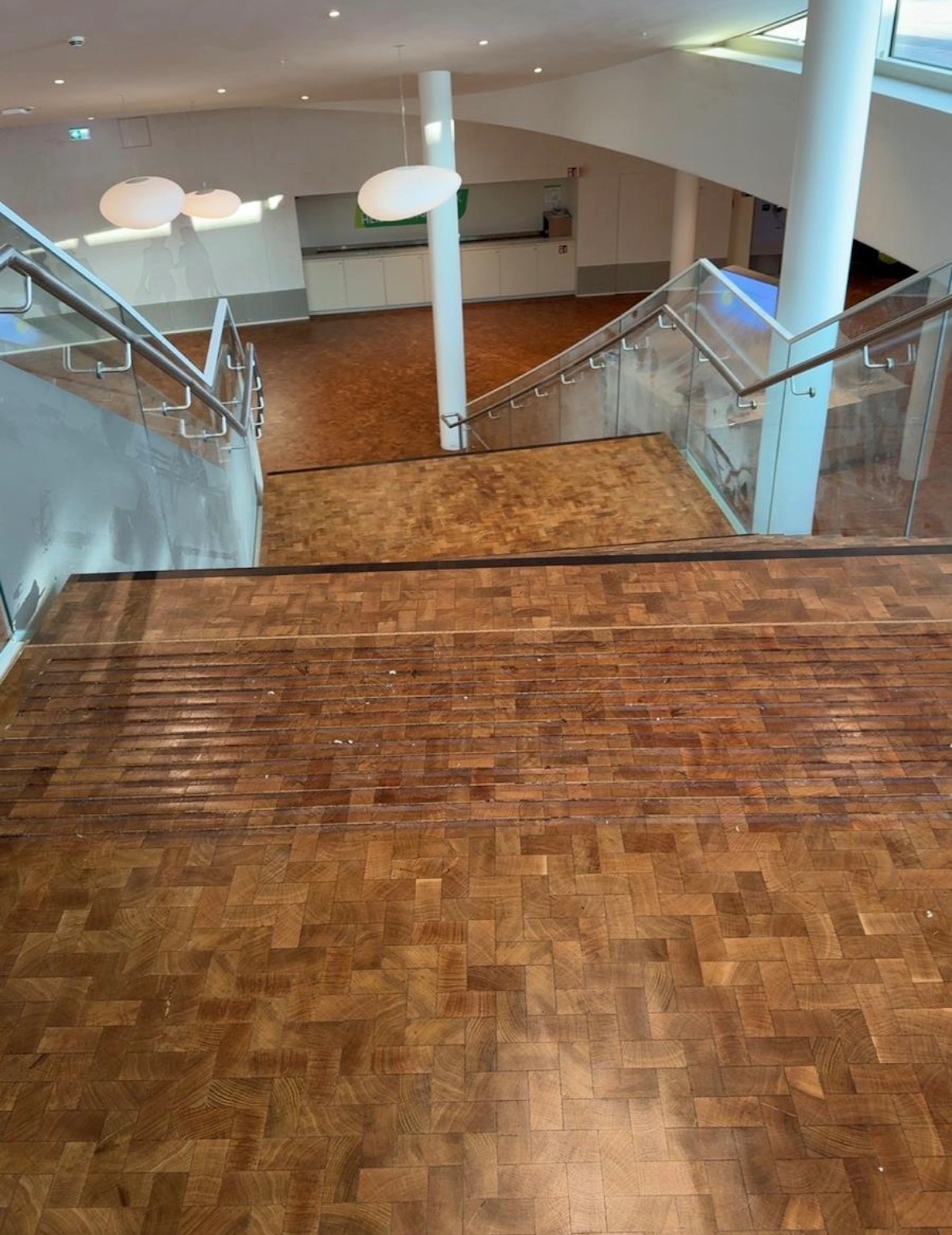 Mit Mosaikparkett belegte Treppe mit Glasgeländer in einem hellen, weiten Treppenhaus