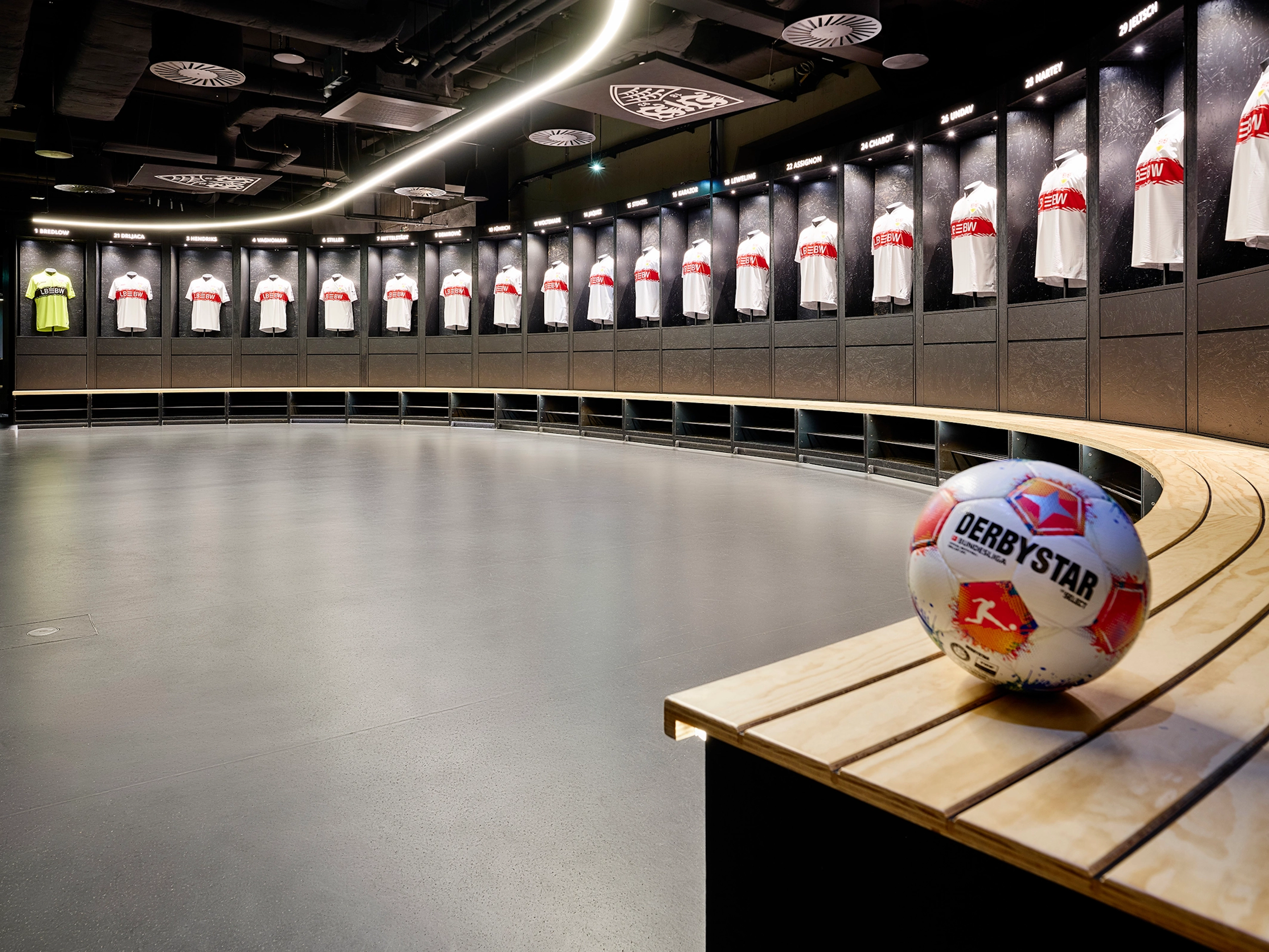 Fachmännisch verlegter, dunkelgrauer Boden in der Umkleidekabine der MHP Arena, gesäumt von schwarzen Spinden mit VfB-Trikots und einem Fußball auf dem Boden.