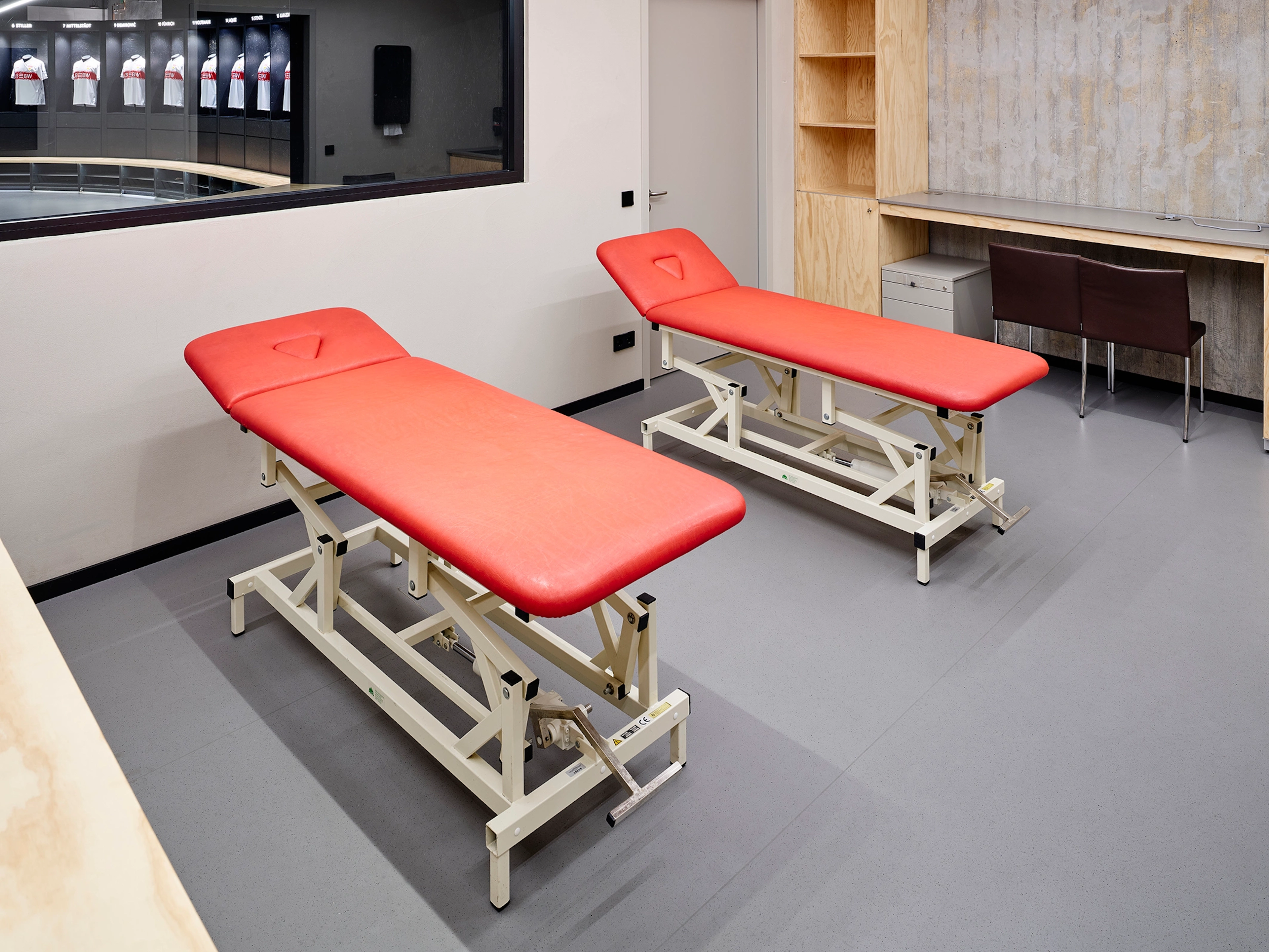 Zwei rote Massageliegen auf einem ebenmäßigen, dunkelgrauen Bodenbelag im Physiotherapie-Raum der MHP Arena Stuttgart.