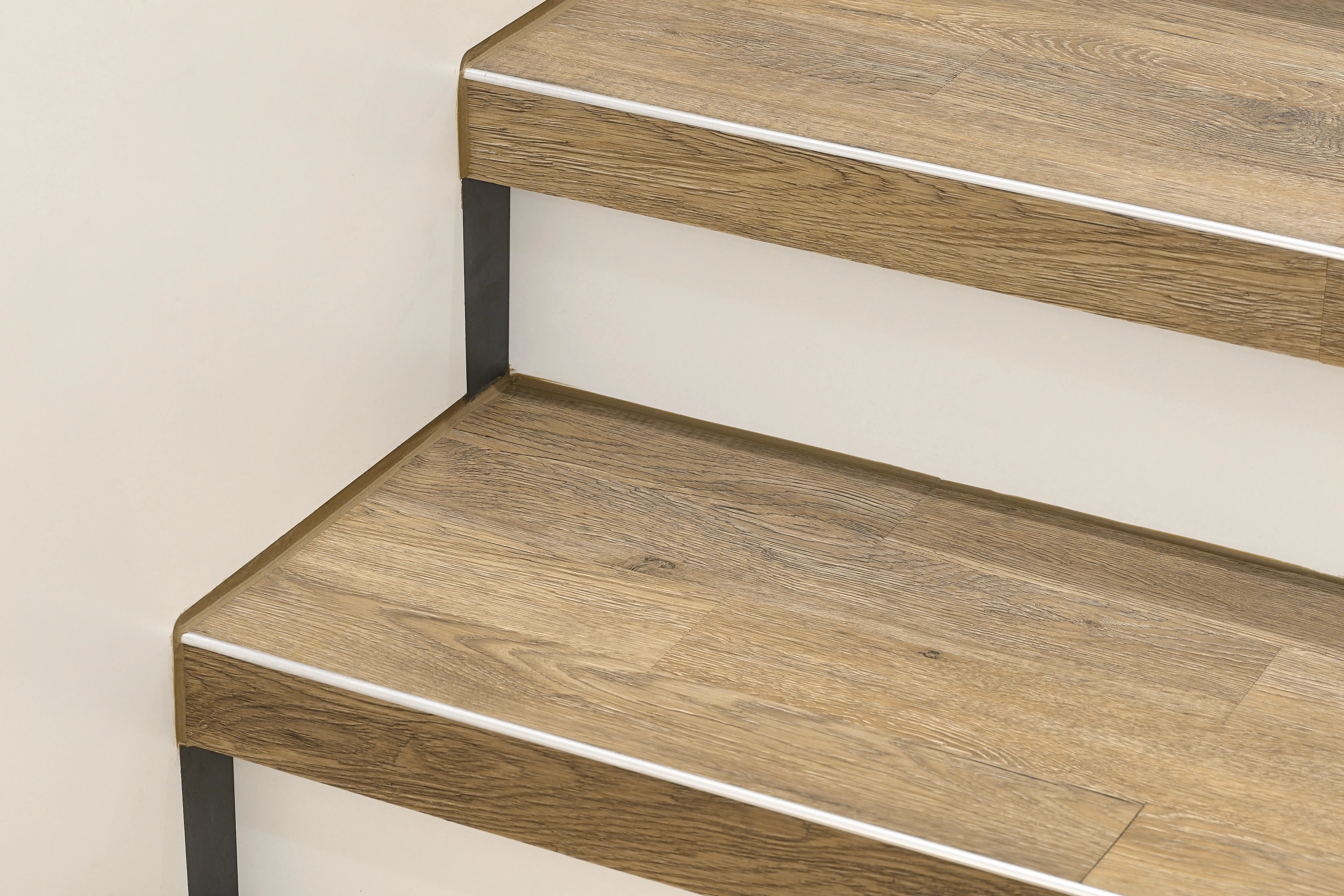 Detailansicht einer Treppensanierung von Parkett Saussele: Mit robustem Vinyl in Holzoptik verkleidete Treppenstufen, kombiniert mit weißen Setzstufen und präzisen Kantenprofilen.