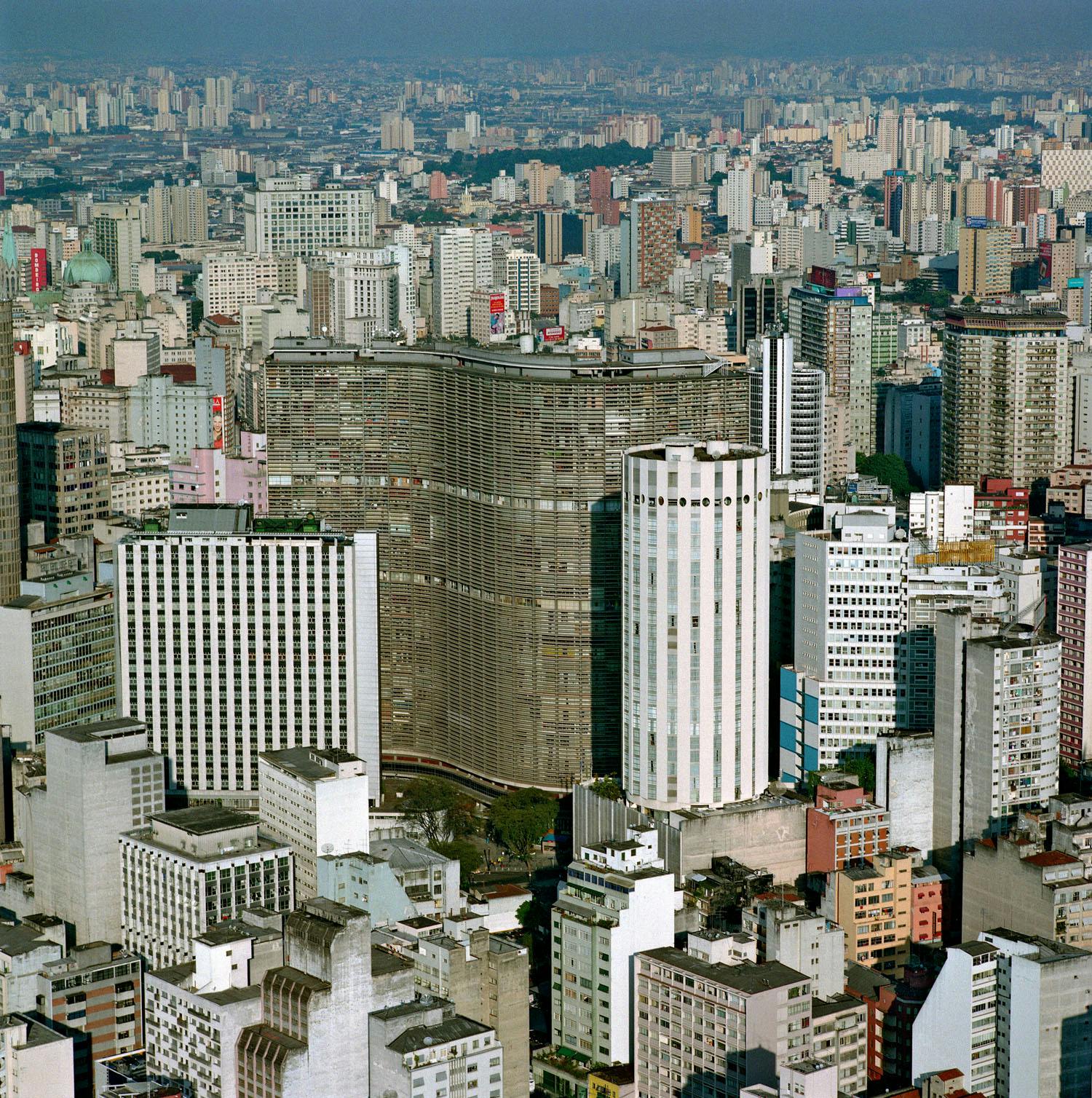 Edifício Copan stands in striking contrast to the surrounding urban landscape of São Paulo with its distinctive, undulating facade amidst the more conventional, rectangular buildings.