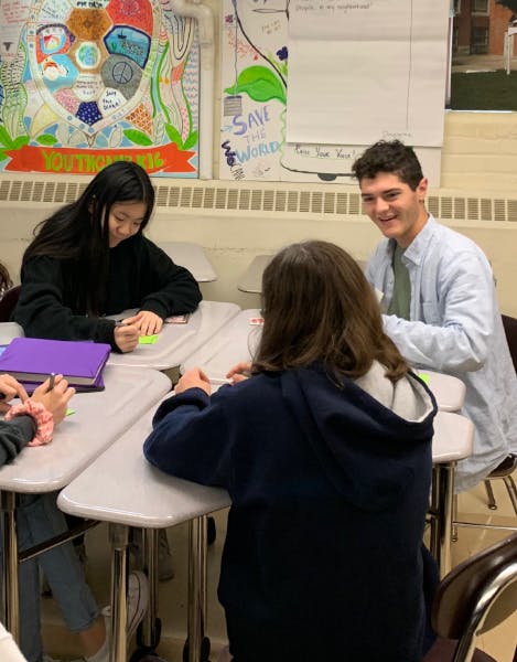 A Scout Labs team member sitting at a group of desks, engaged in conversation with a young student