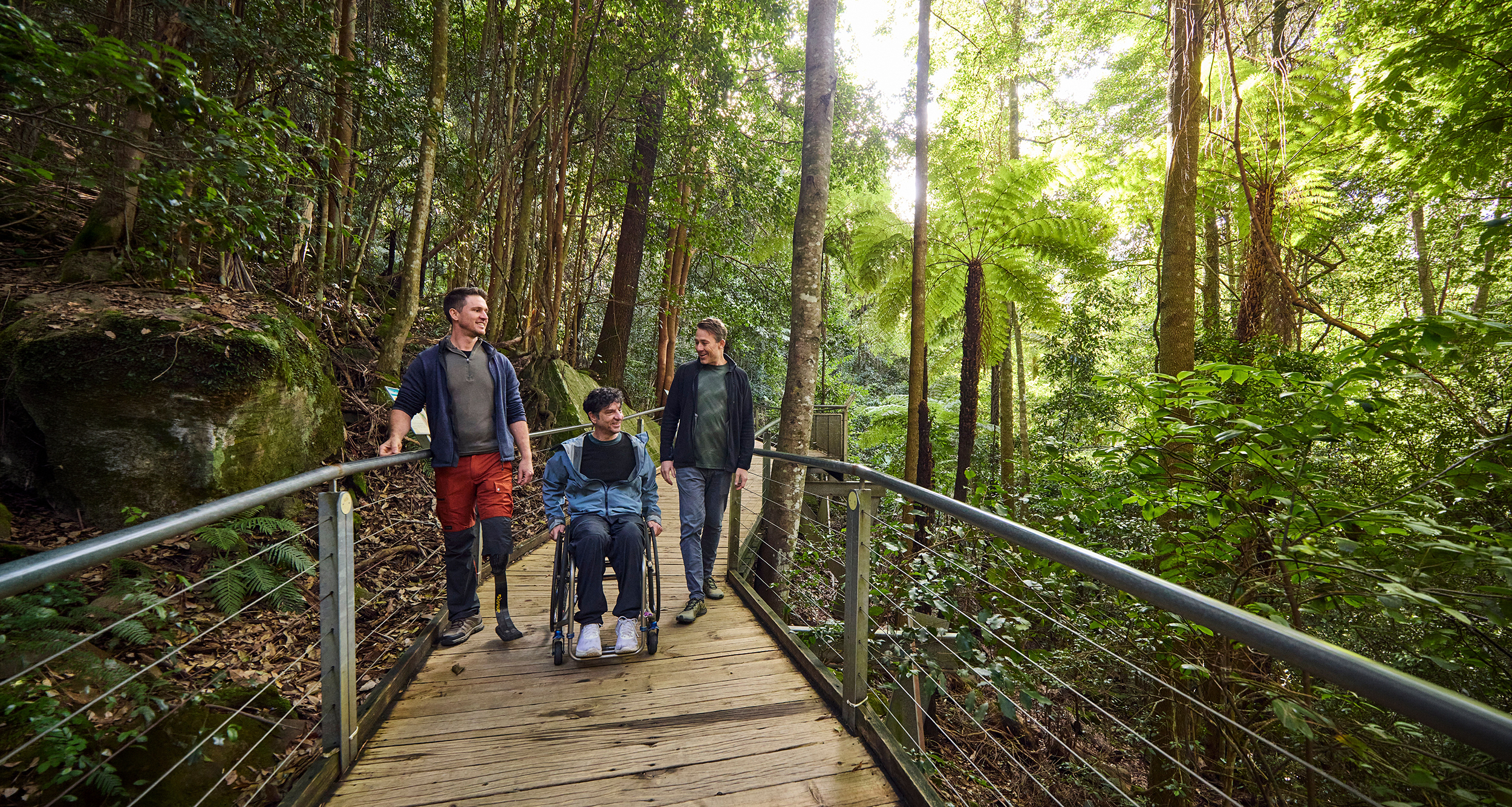 Three people with accessibility needs on the Scenic Walkway. One in wheelchair, one with prothesis