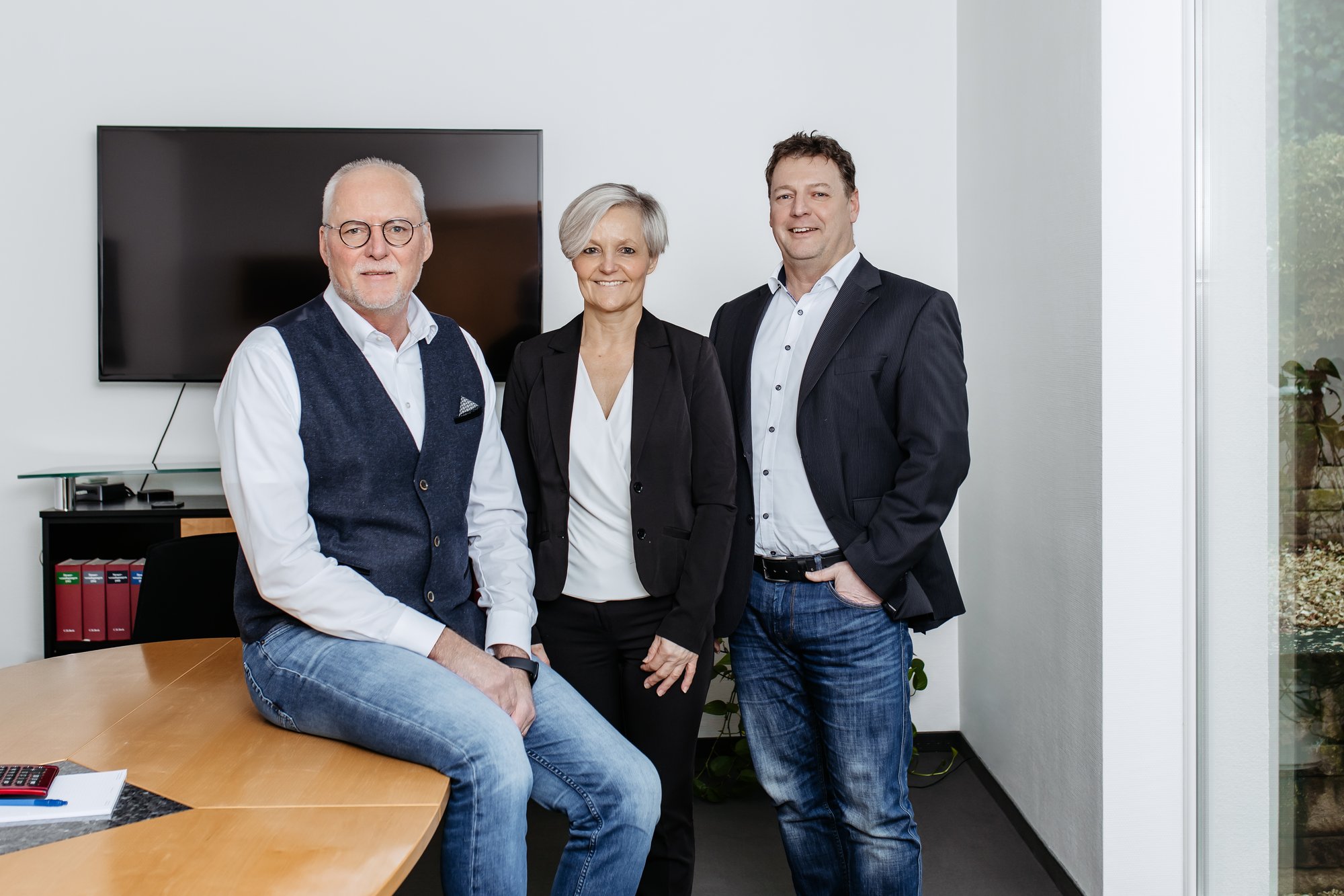 Team der Steuerkanzlei sup.tax im Besprechungsraum – drei Kolleginnen und Kollegen lächeln in die Kamera