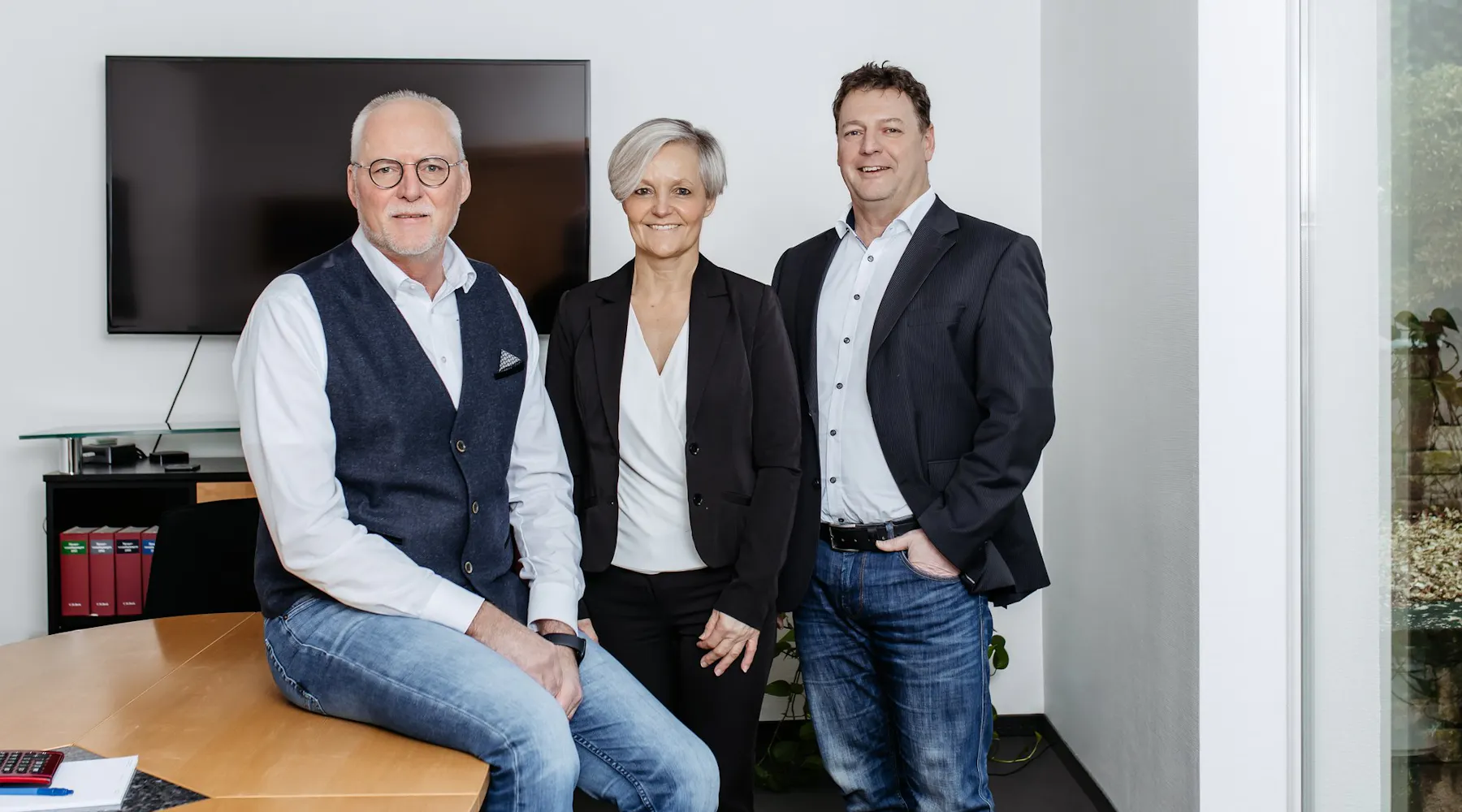 Team der Steuerkanzlei sup.tax im Besprechungsraum – drei Kolleginnen und Kollegen lächeln in die Kamera