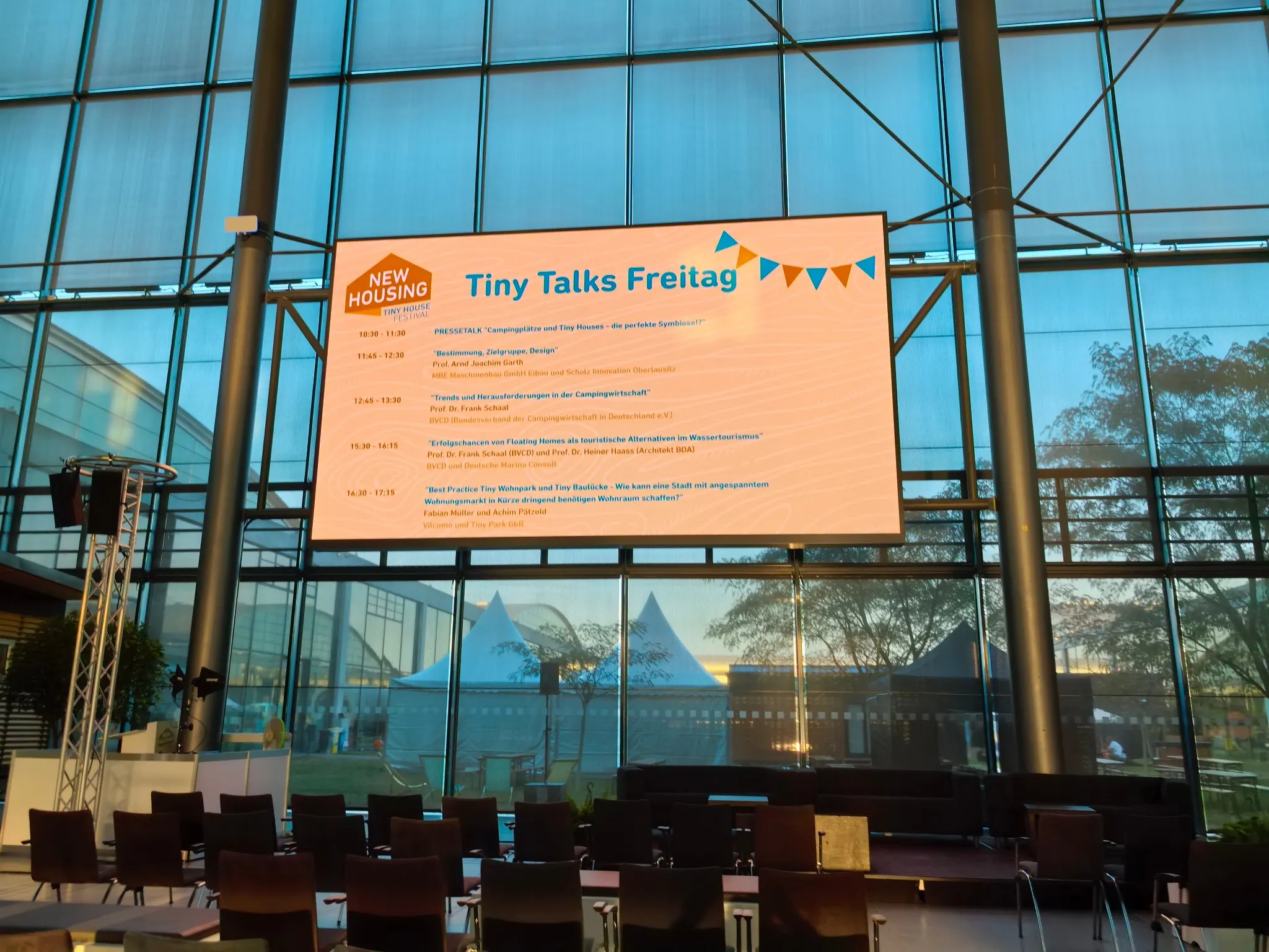 Programm der Tiny Talks auf der Großleinwand der NEW HOUSING 2026