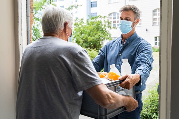 Masked elderly man receiving home food delivery from masked younger man
