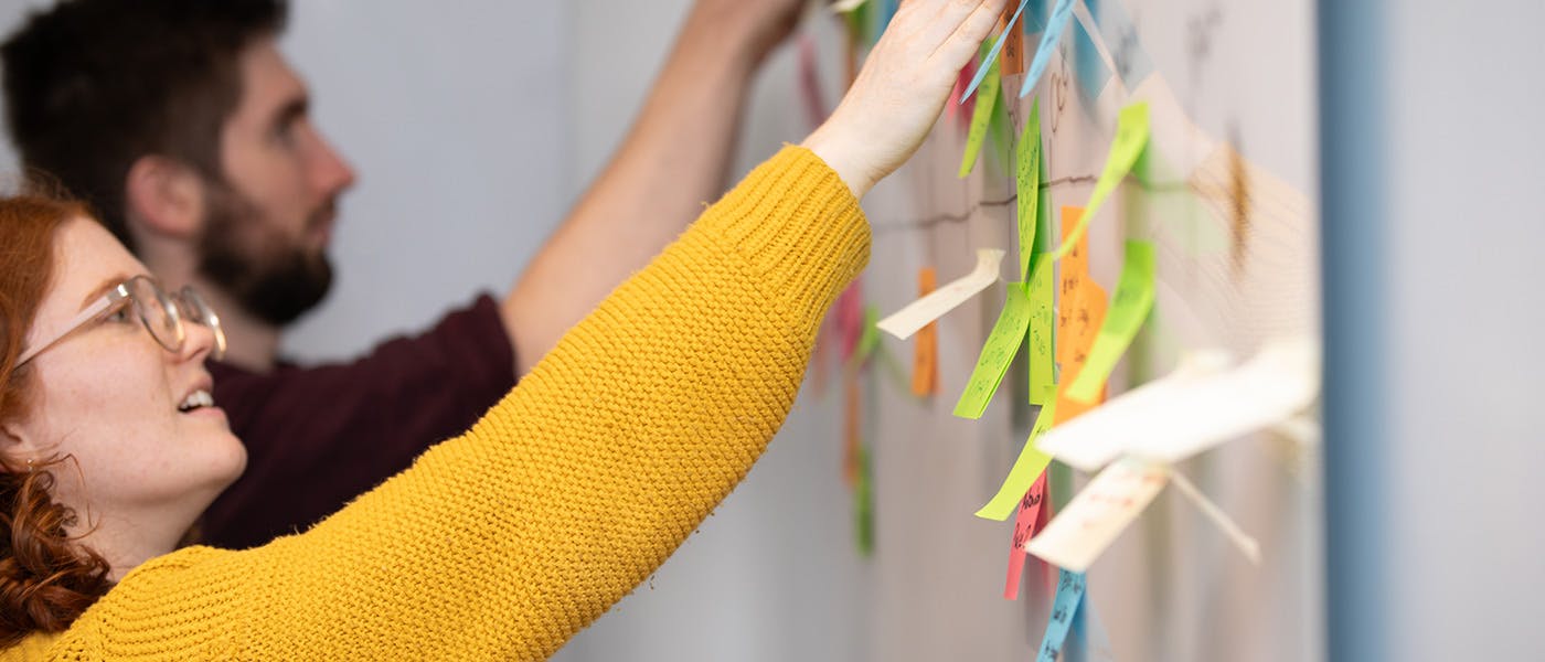Woman and man placing sticky notes on a whiteboard