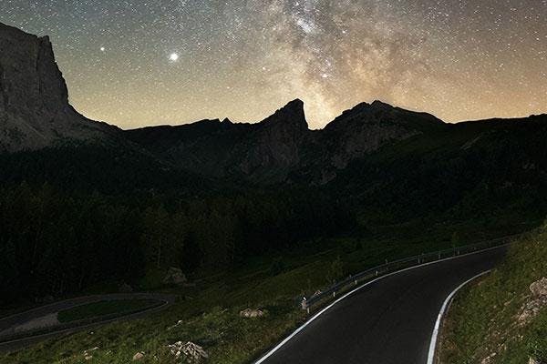 A road curving to the right at night with a starry sky above