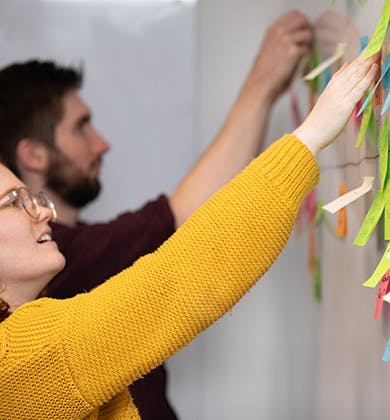 Woman and man placing sticky notes on a whiteboard