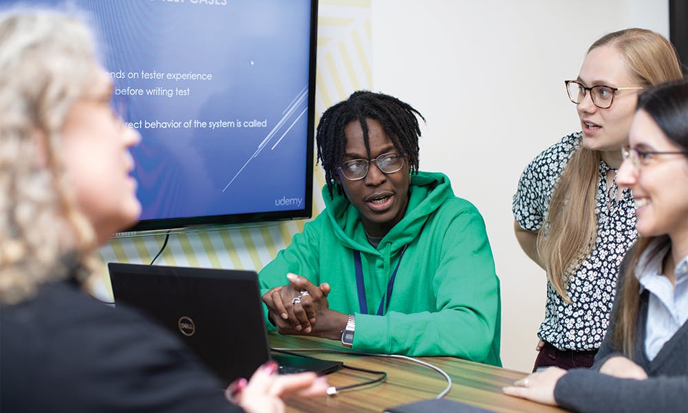 Meeting around laptop with large screen on the wall behind