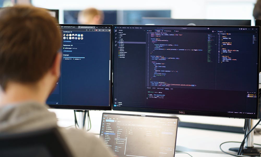 Person looking at monitors and laptop with code on screen