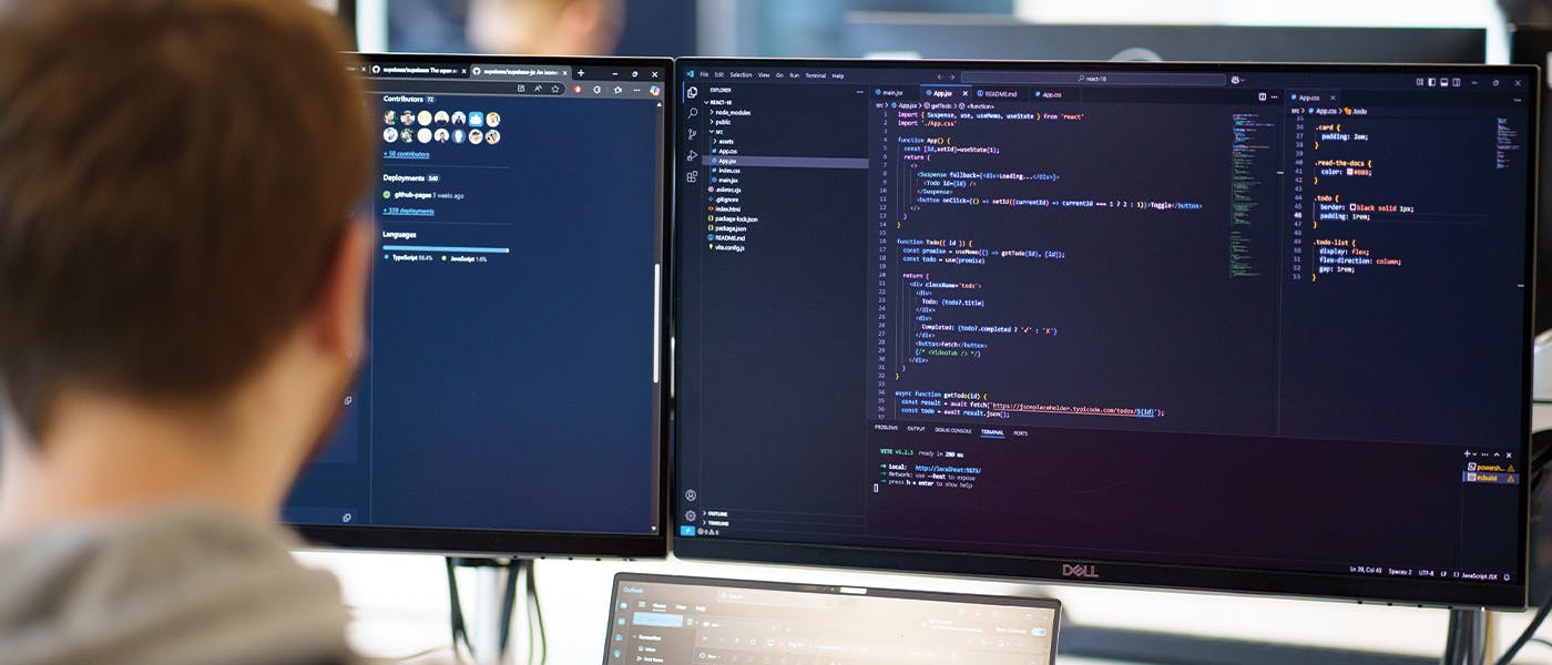 Person looking at monitors and laptop with code on screen