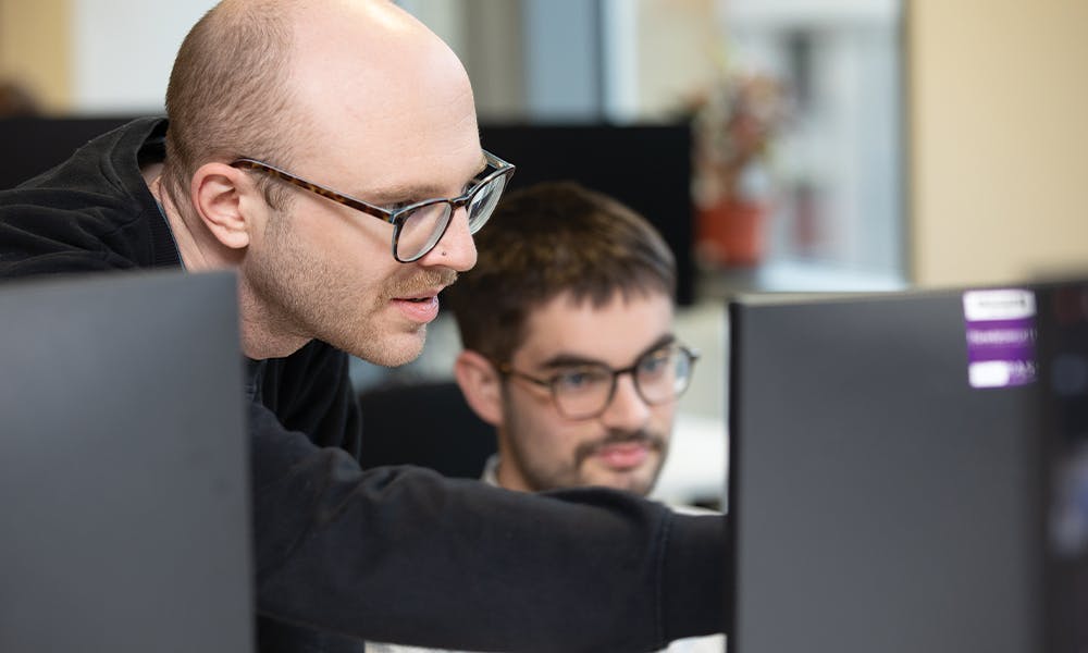 Two people discussing some computer code, with one person pointing at the screen