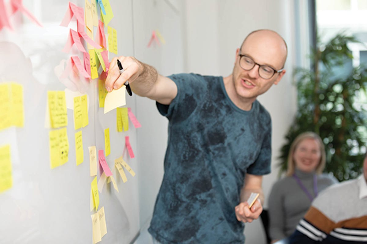 Person puts sticky note on board during a meeting