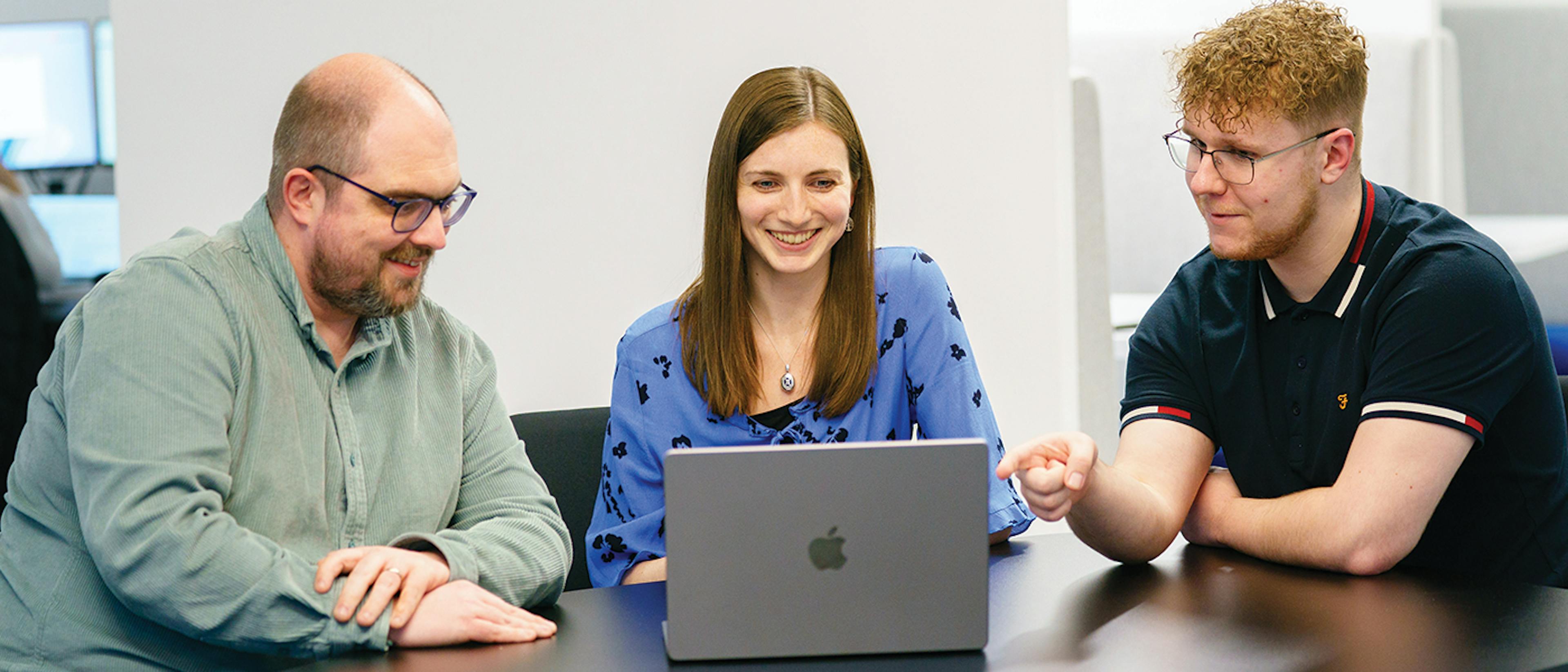 Three people sat at a desk around a laptop