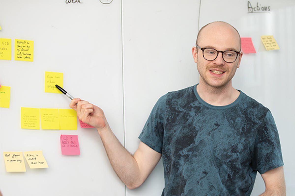 Person pointing at sticky note on a white board