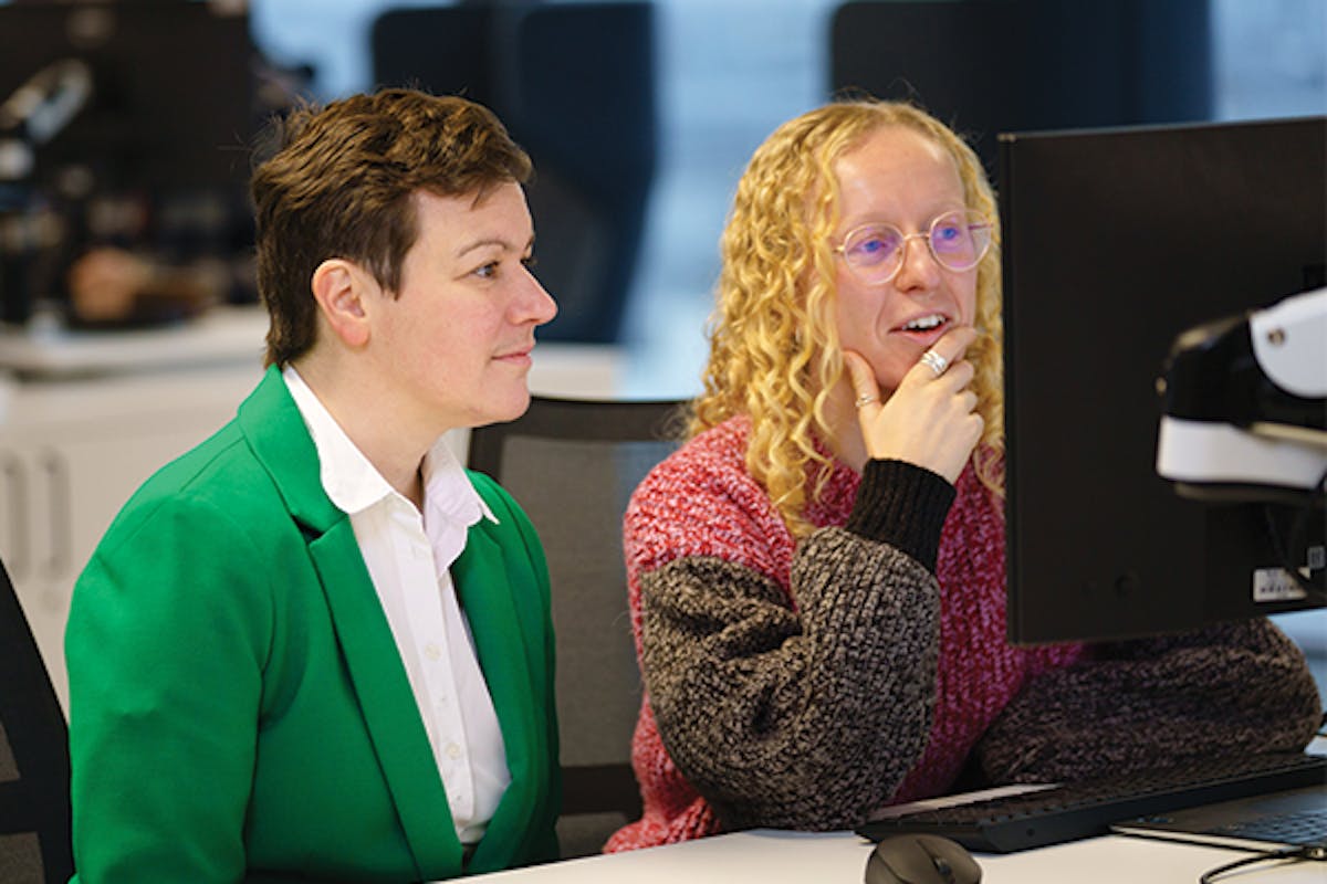 Two people sitting behind a desk looking a computer monitor