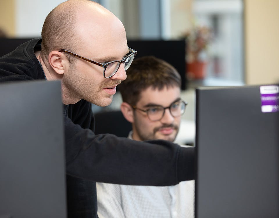 Two people discussing some computer code, with one person pointing at the screen
