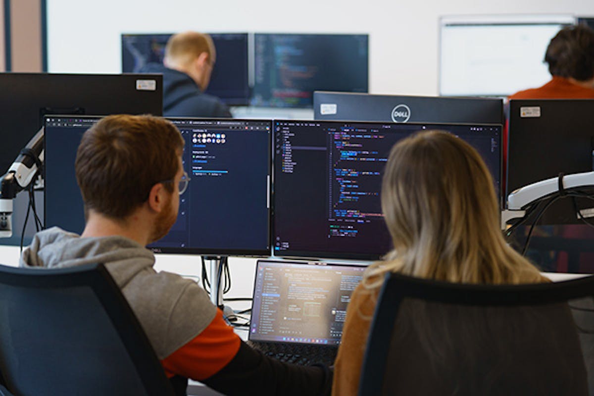 Two people pair programming in front of three screens