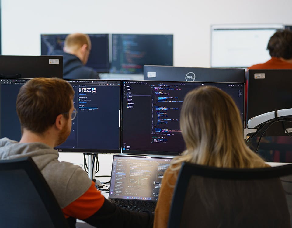 Two people pair programming in front of three screens