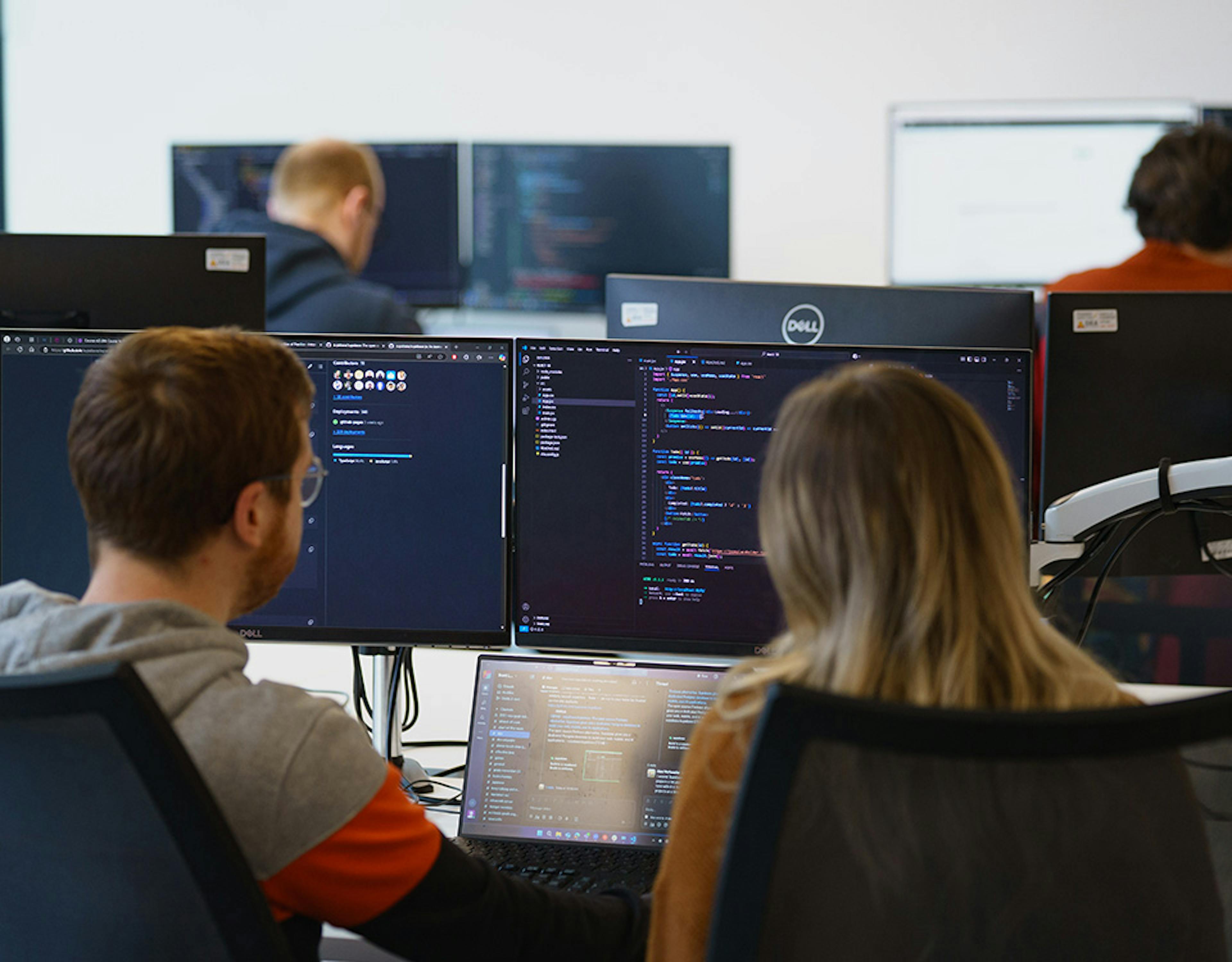 Two people pair programming in front of three screens