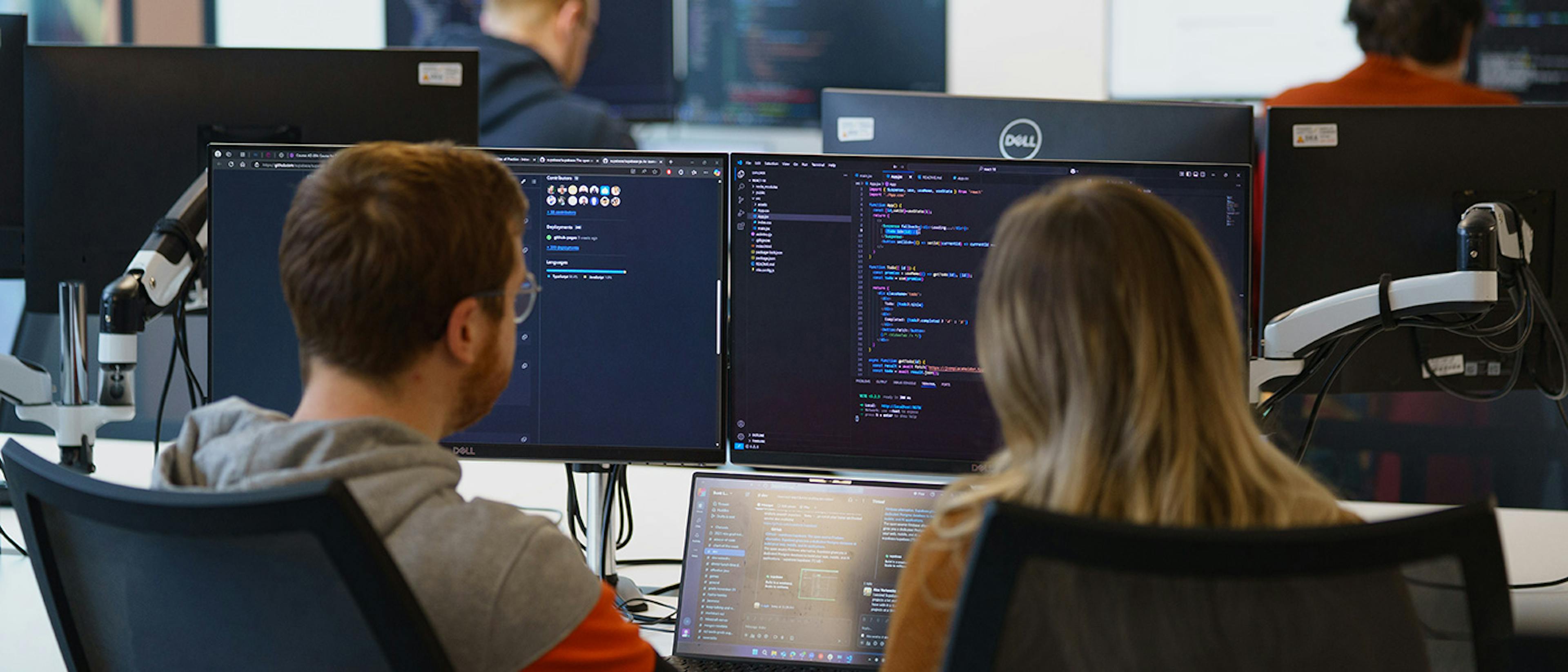 Two people pair programming in front of three screens