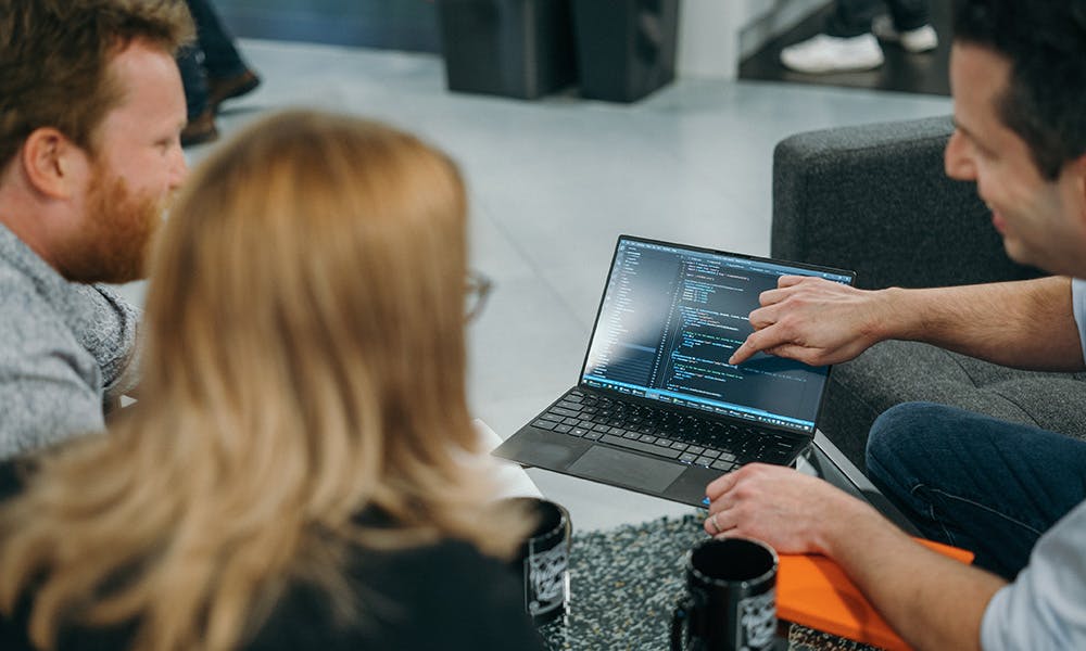 Three people looking at some code on a laptop