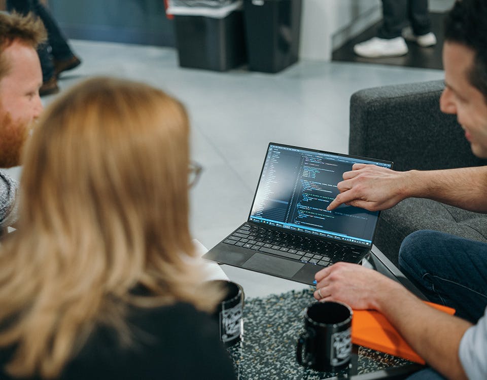 Three people looking at some code on a laptop
