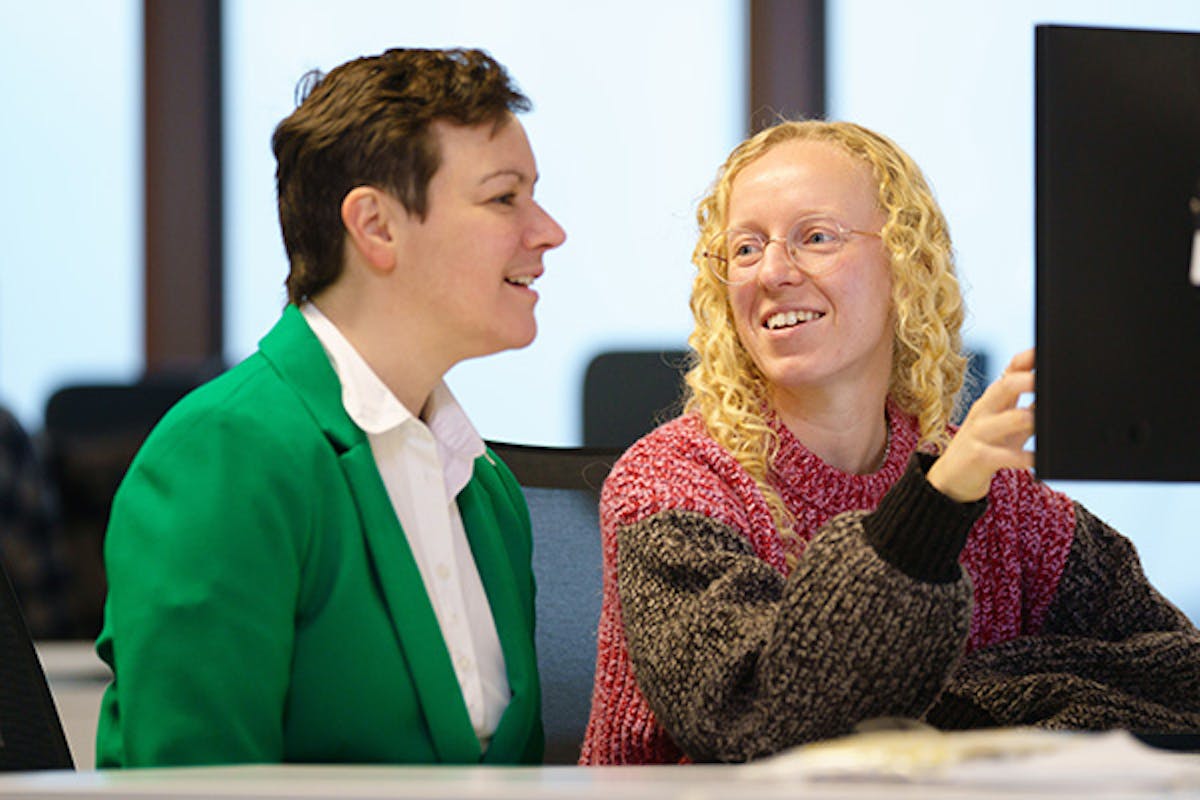 Two people at a desk discussing something displayed on a computer screen