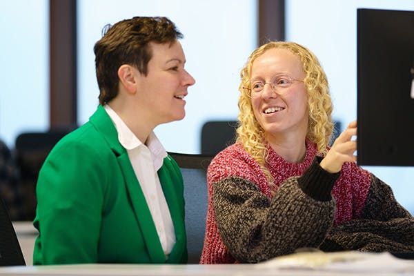 Two people at a desk discussing something displayed on a computer screen