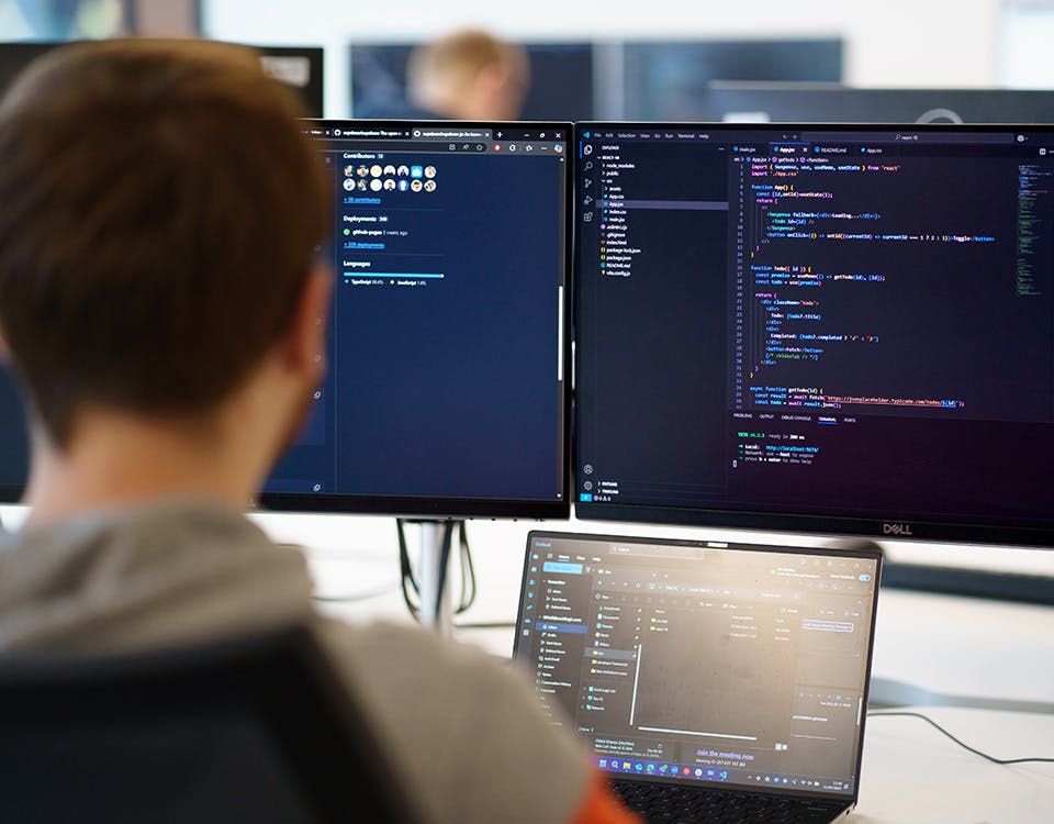 Person looking at monitors and laptop with code on screen