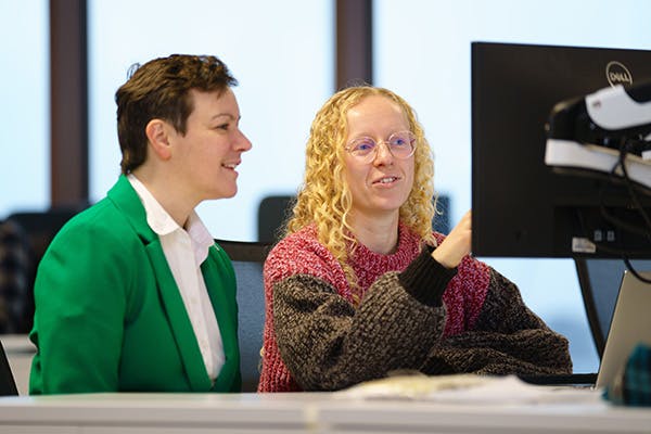 Two people at a desk discussing something displayed on a computer screen