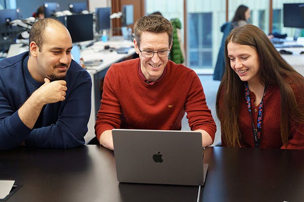 Three people in a meeting, looking at a laptop screen