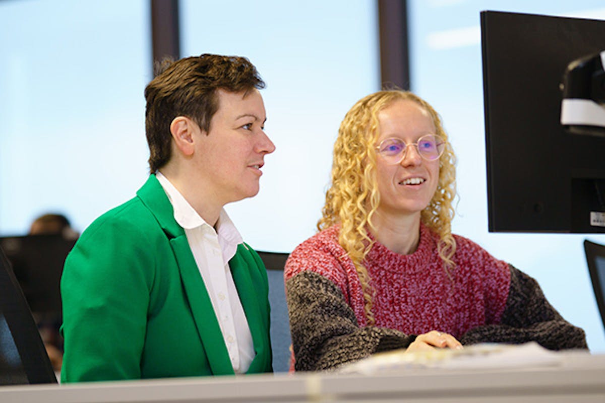 Two women working at a desk in an office, discussing something on the screen