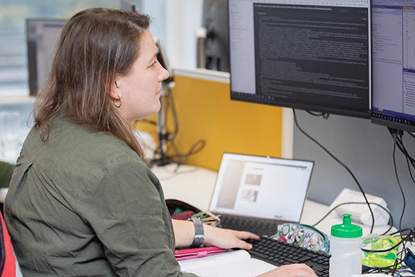 Woman working at a desk with three screens