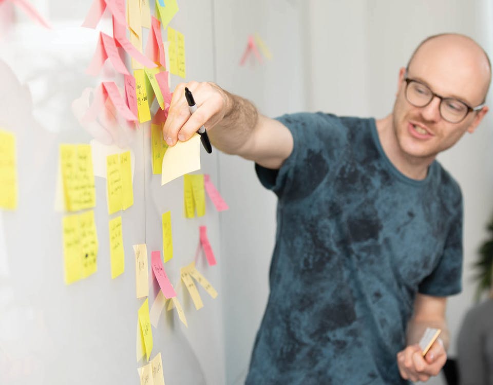 Man in a meeting adding a sticky note to a white board