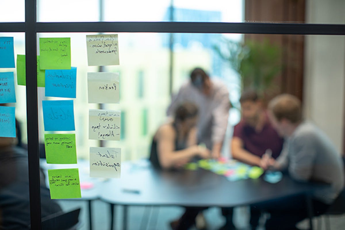 People around a table in a workshop meeting with sticky notes on the window