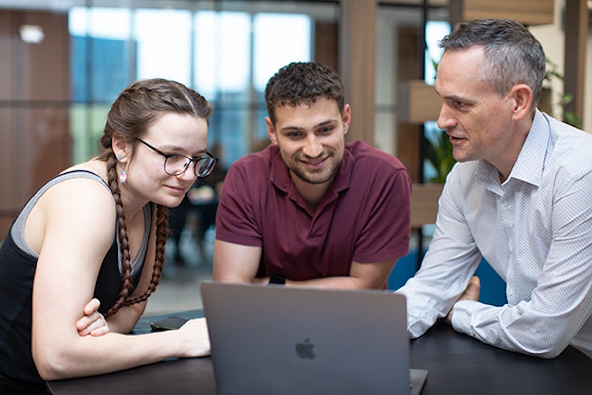 Three people in a meeting looking at a laptop