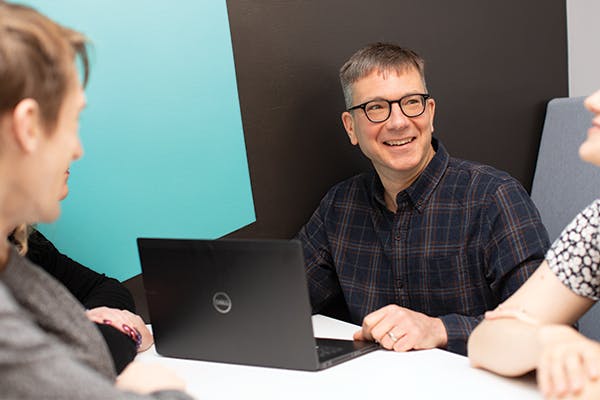 Four people in a meeting, with a man with a laptop smiling at his colleagues