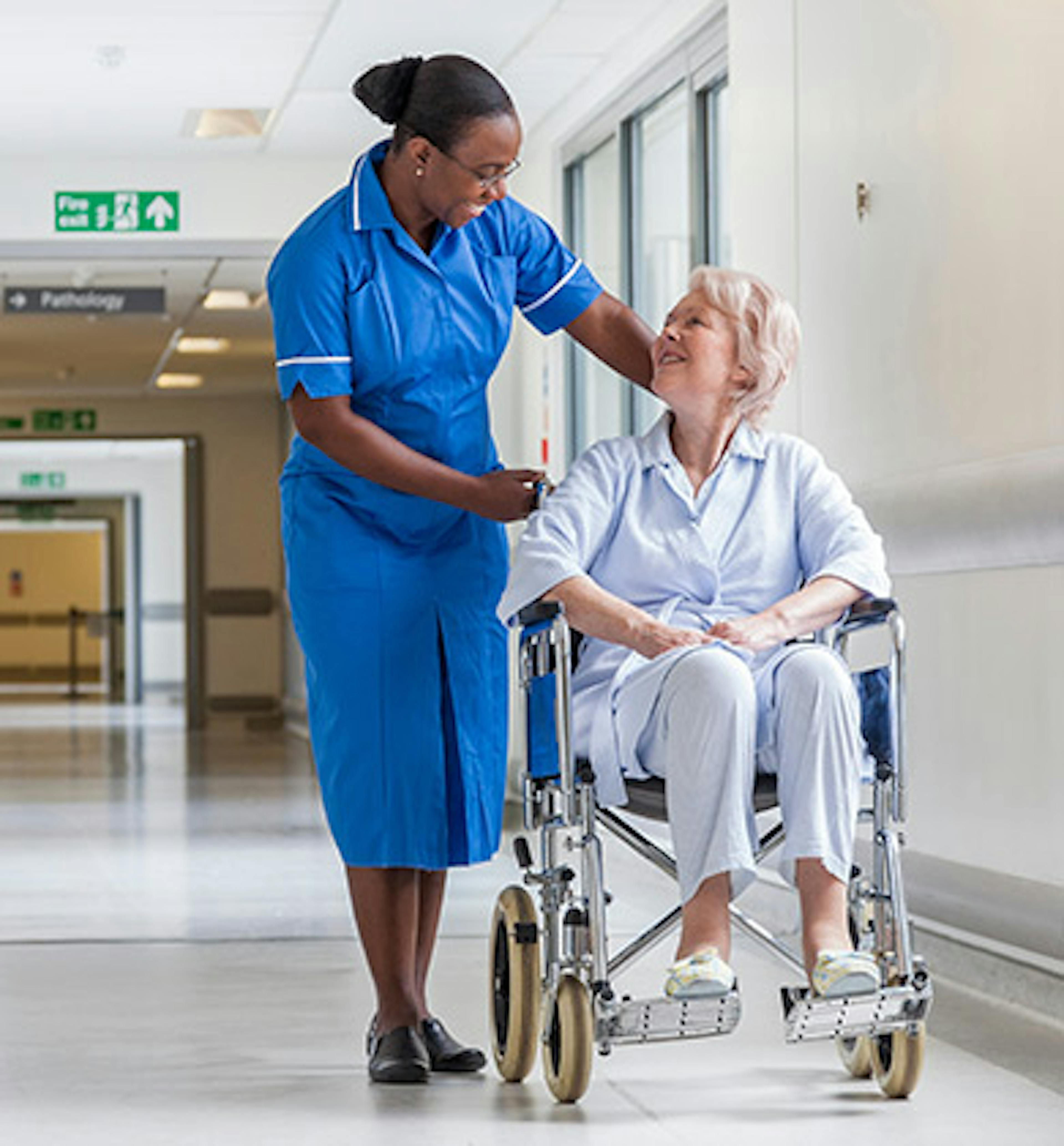 People in a hospital corridor, with a nurse and doctor talking on the left, and a nurse with a patient in a wheelchair on the right