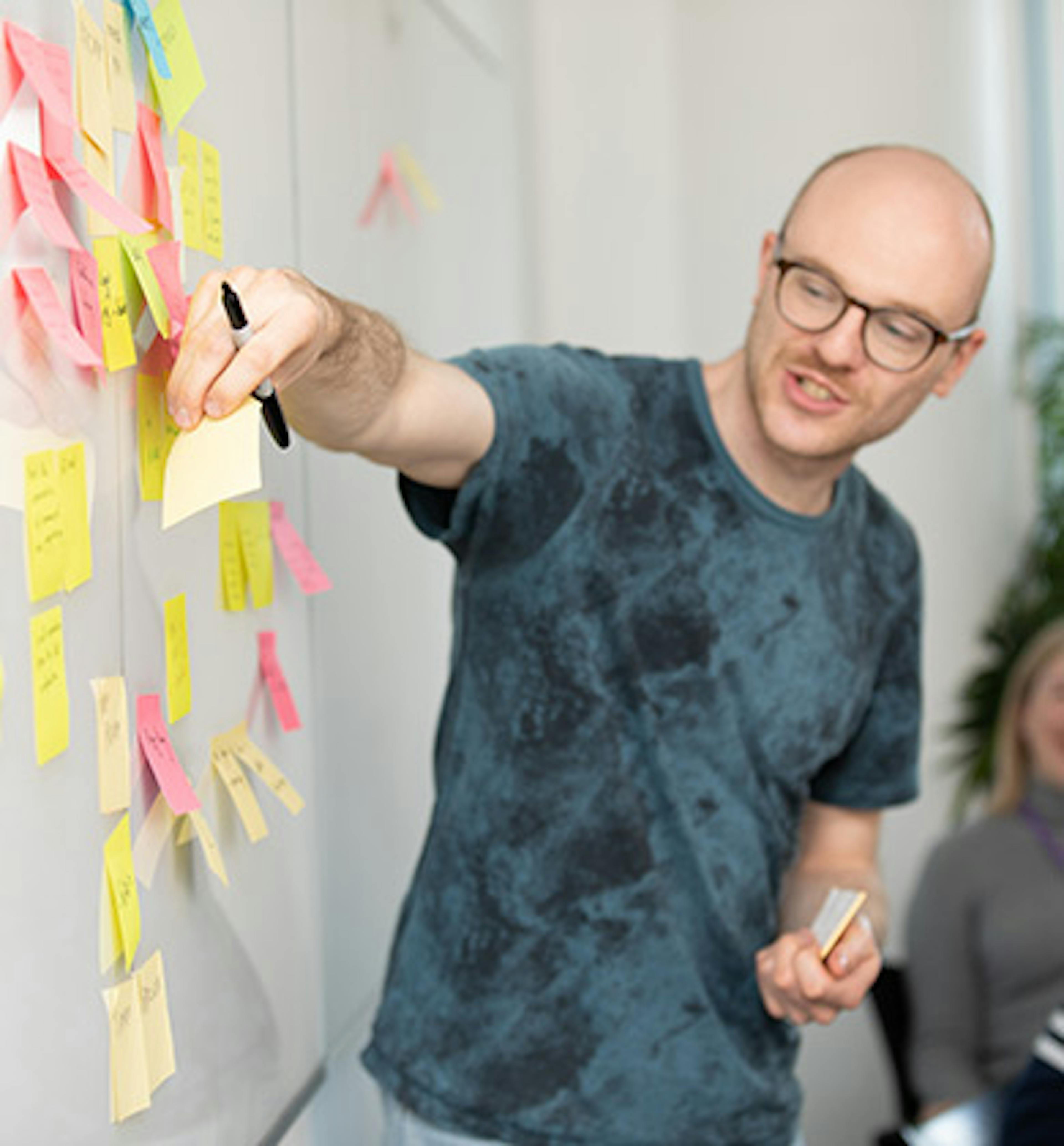 Man in a meeting adding a sticky note to a white board