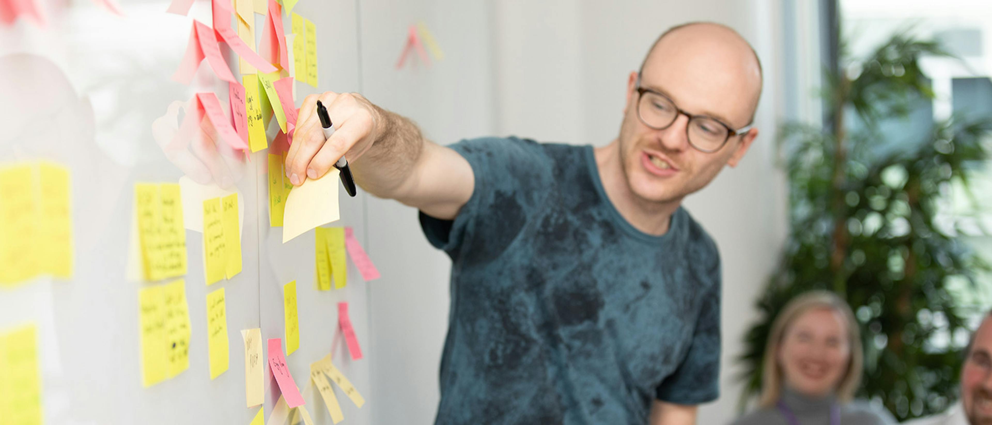 Man in a meeting adding a sticky note to a white board