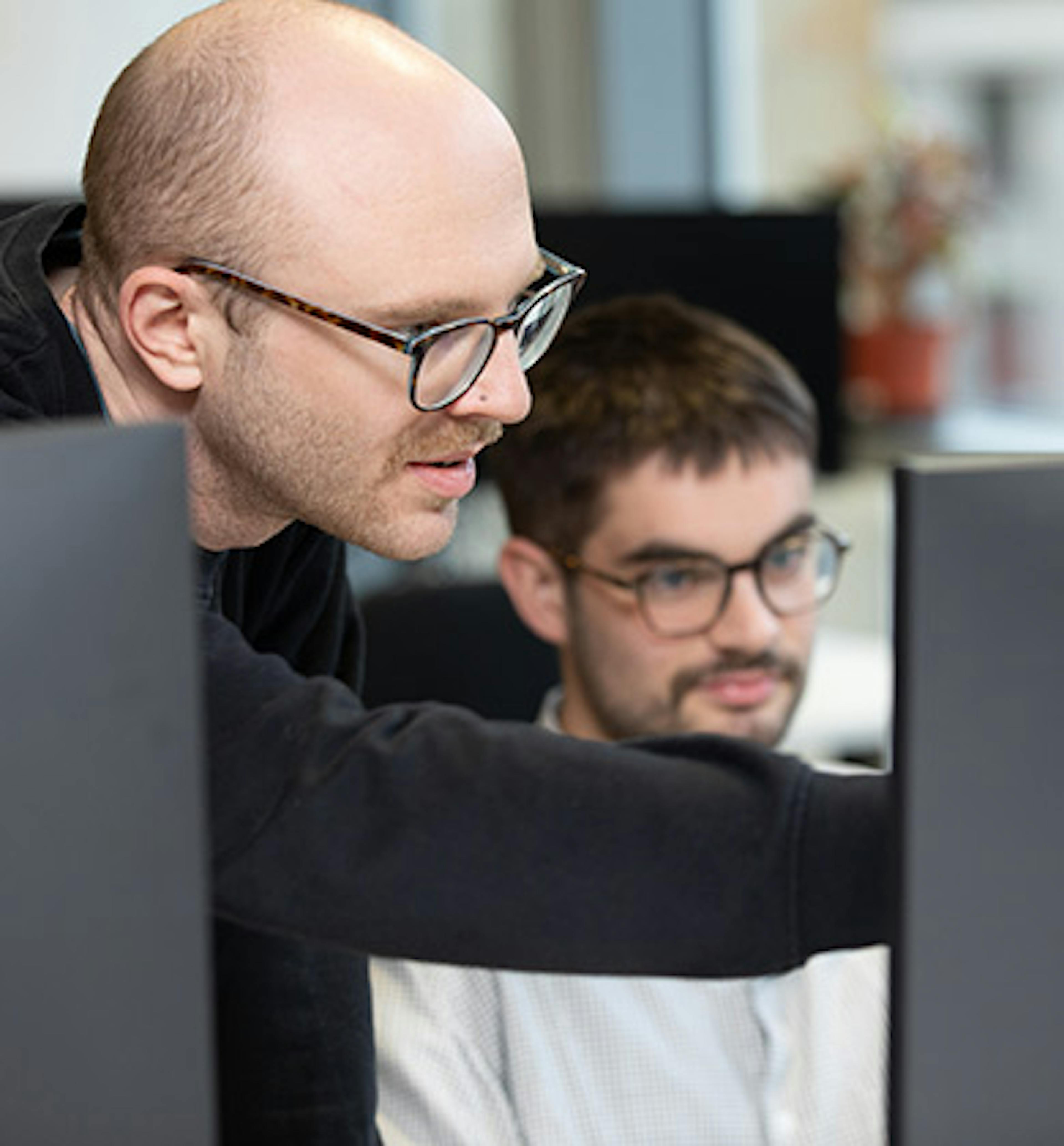 Two people discussing some computer code, with one person pointing at the screen