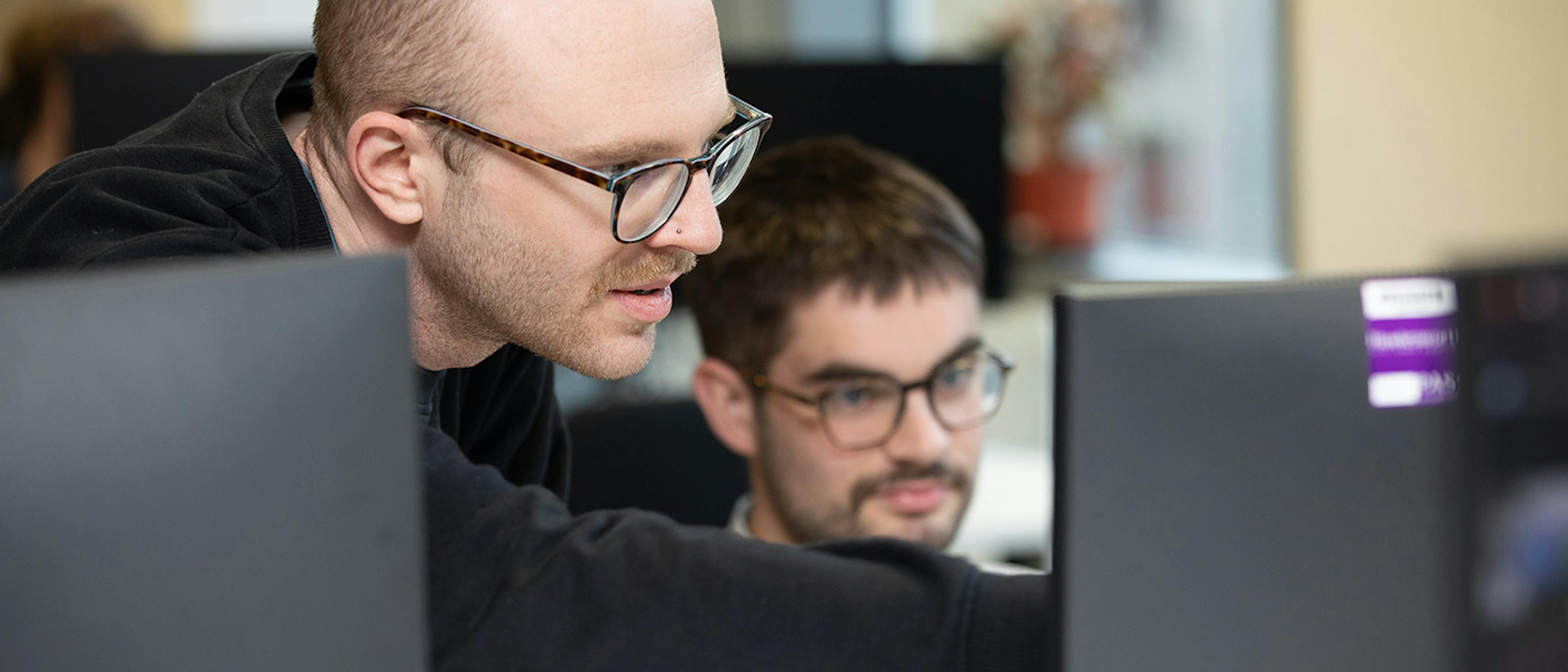 Two people discussing some computer code, with one person pointing at the screen