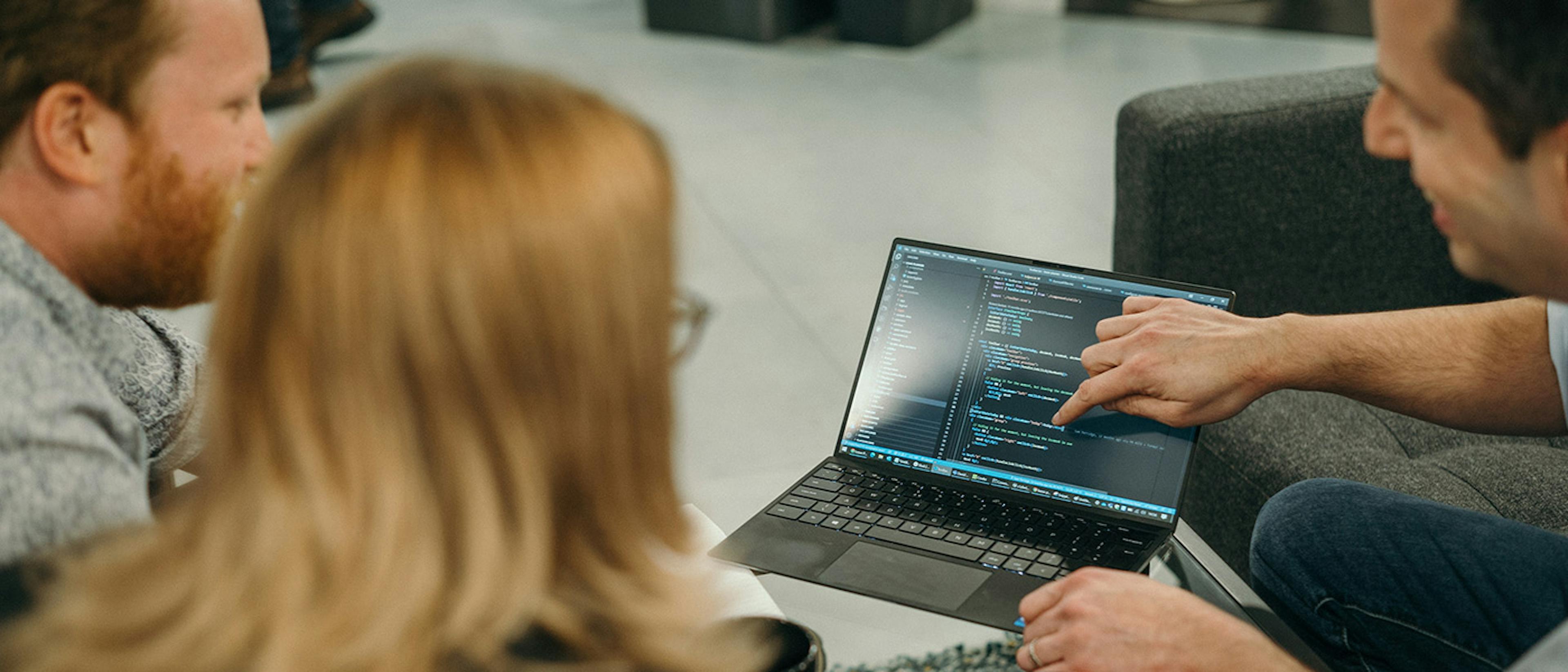 Three people looking at some code on a laptop