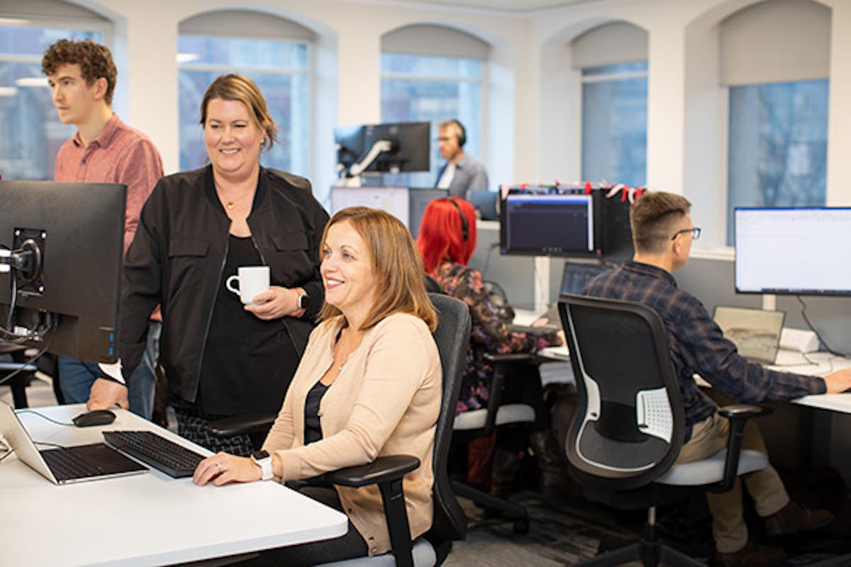 People working in an office, with two women in the left foreground looking at a computer screen